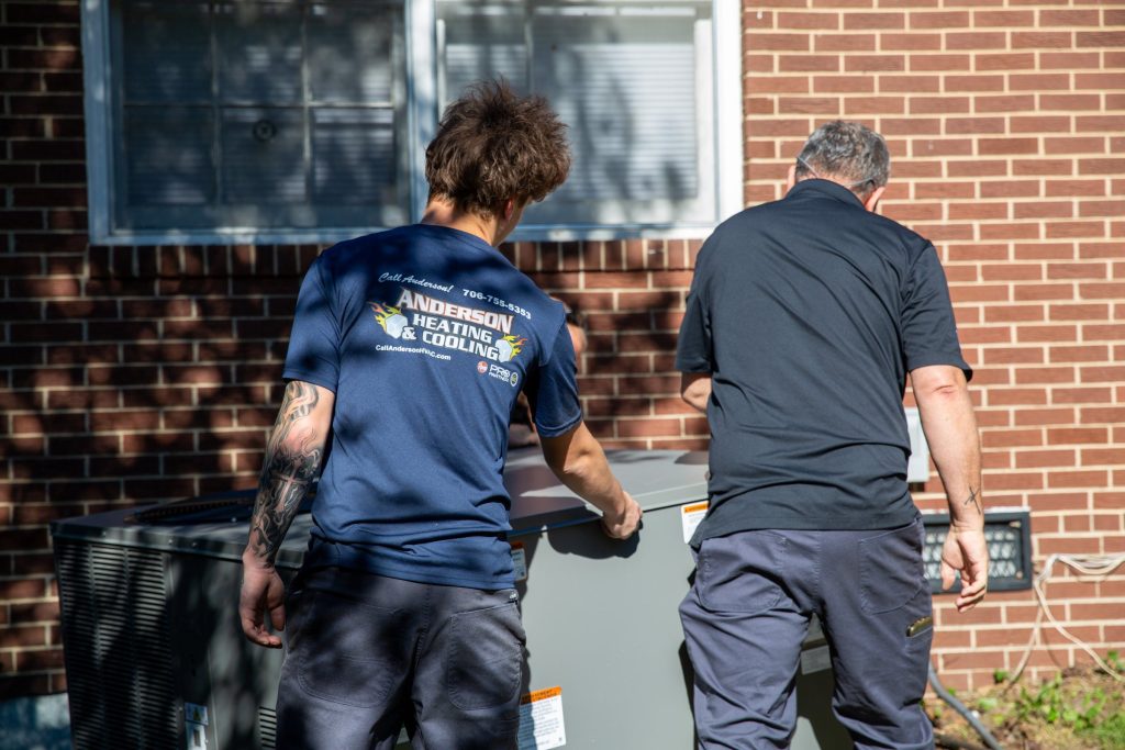 Anderson Heating & Cooling technicians setting a new HVAC unit at a brick home